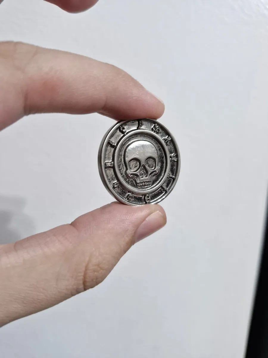 Moeda de metal com caveira lisa em relevo, cercada por runas