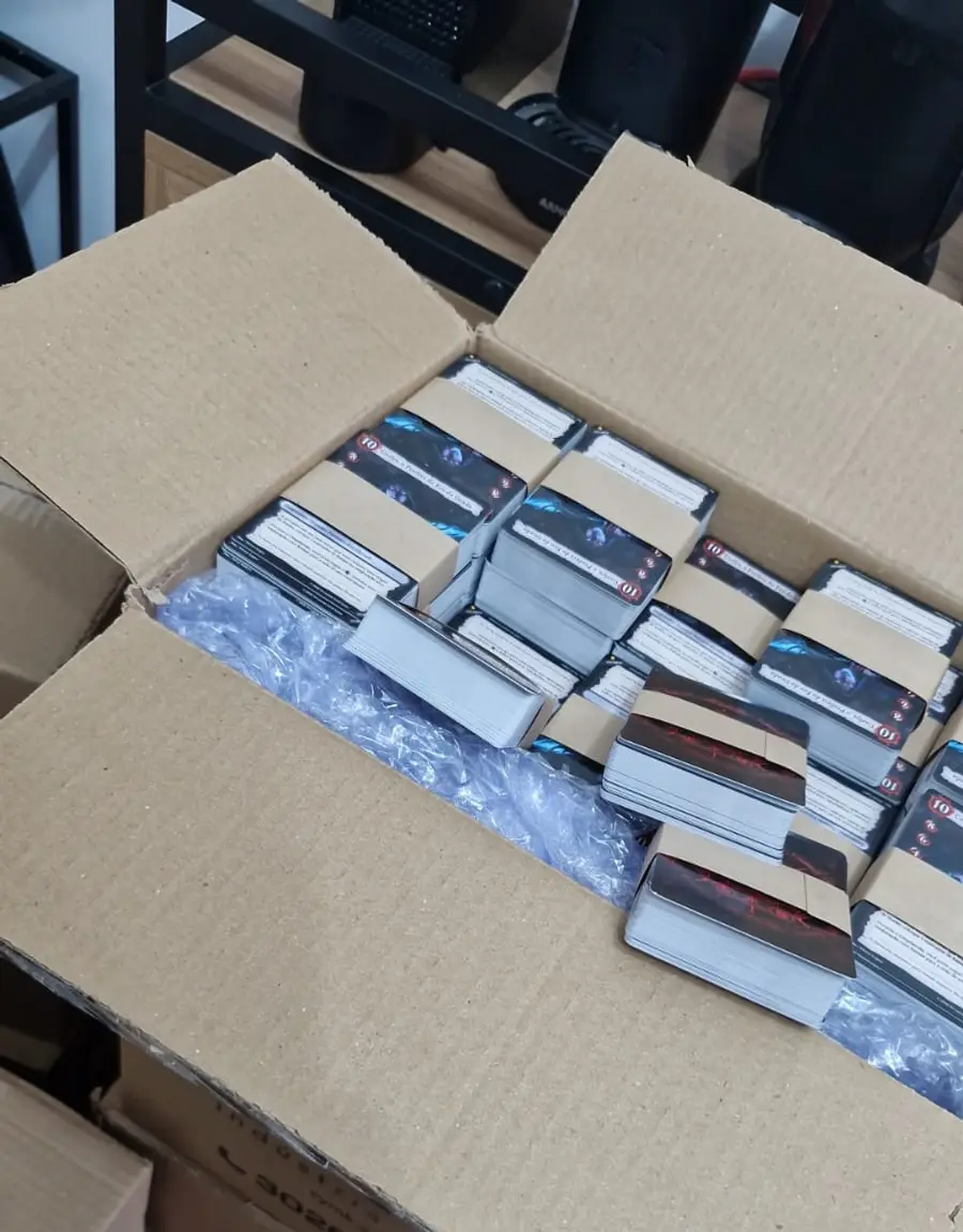Caixa de papelão aberta com dezenas de blocos de cartas do Arcanum cintados e organizados
