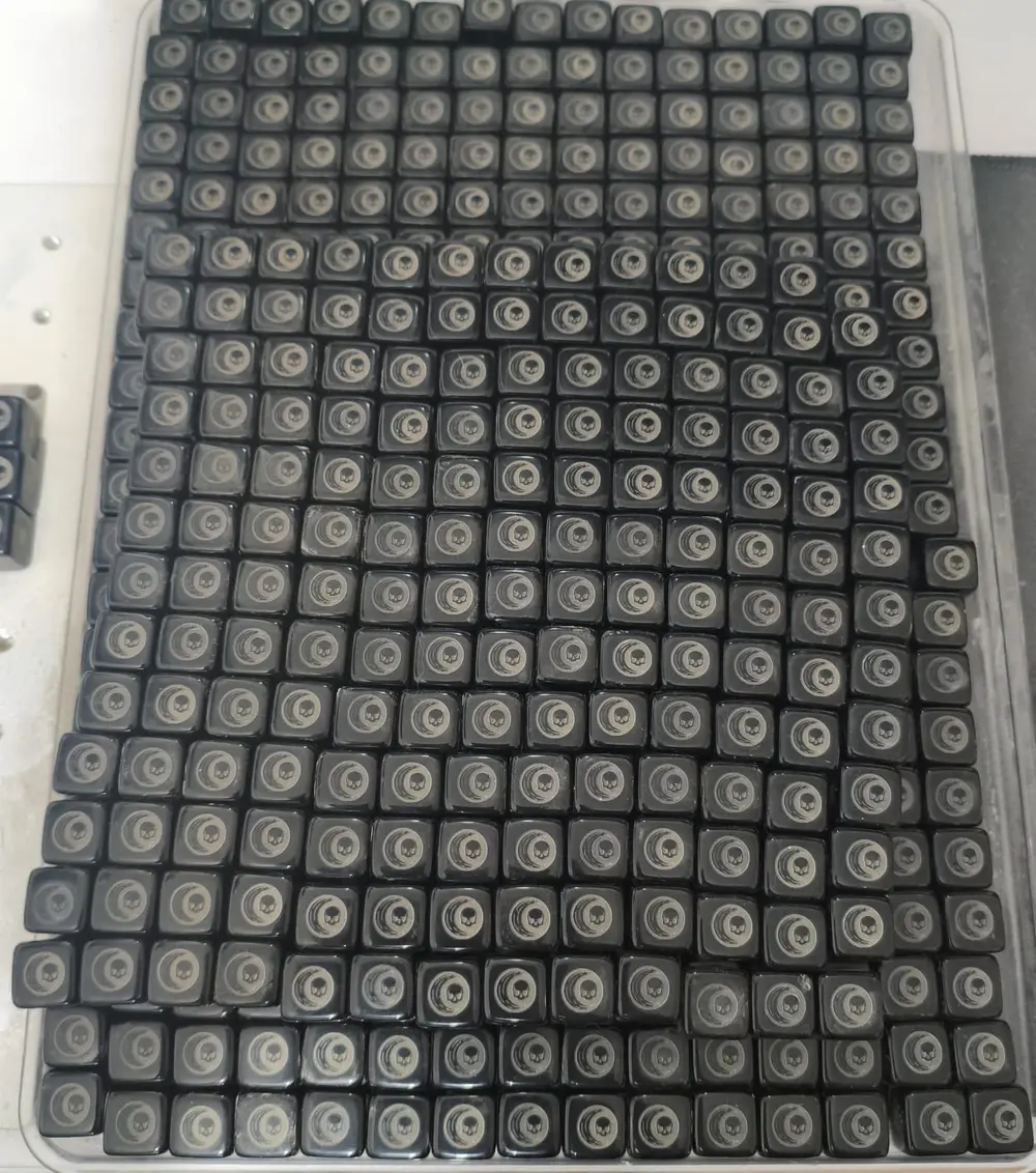Bandeja com centenas de dados pretos do Arcanum, com o símbolo gravado na face