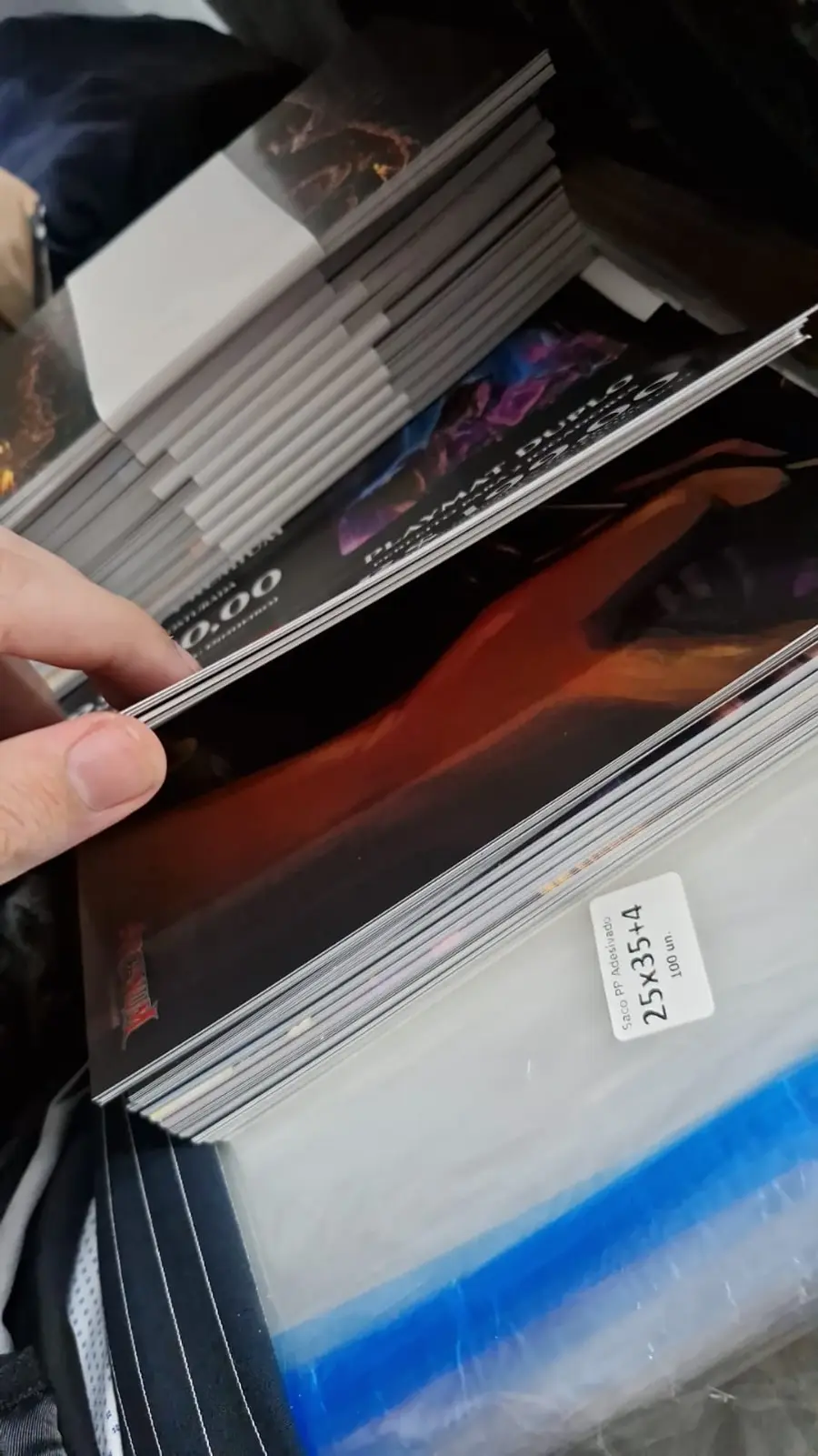 Stack of Arcanum playmats with printed art, next to their plastic wrapping
