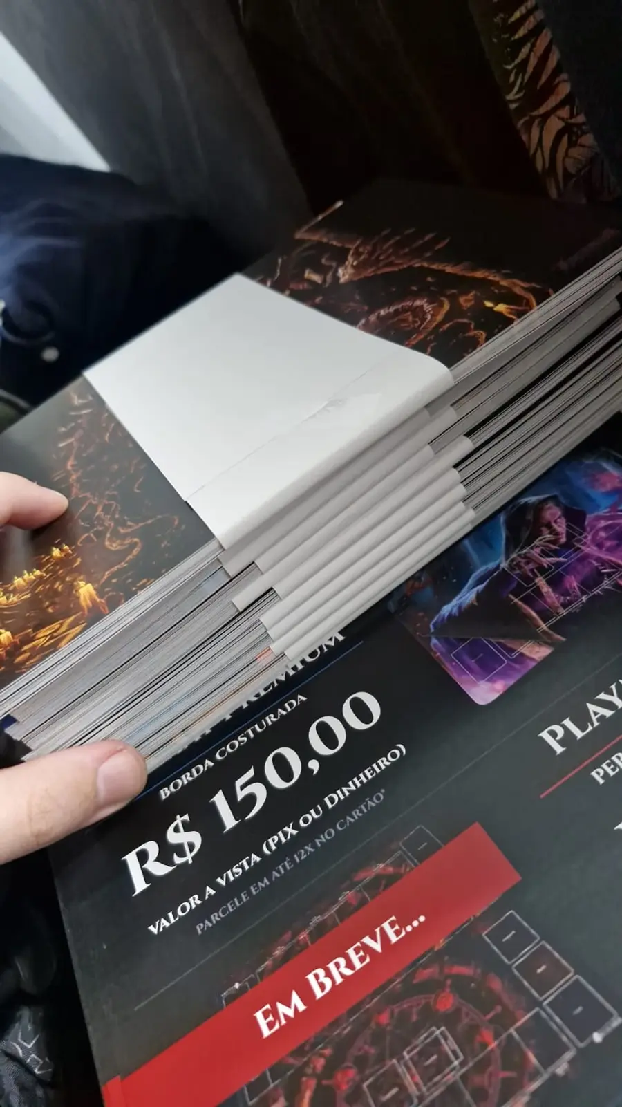 Material promocional impresso do Arcanum segurado na mão, com arte de dragão ao fundo